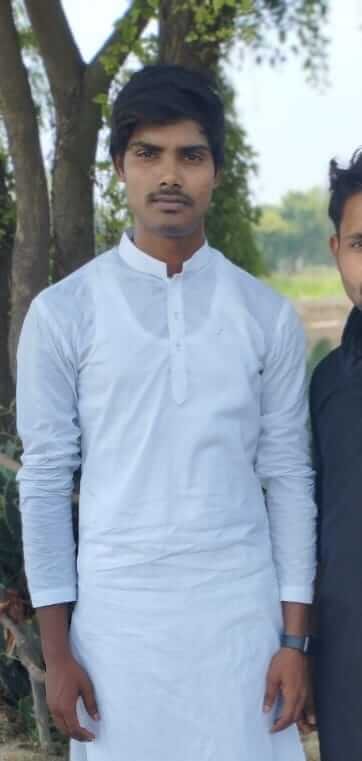 Man standing under a tree in a farm field wearing white traditional clothes
